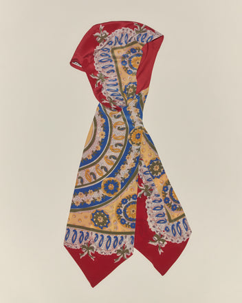 The Bricolage Driving Cap is perfectly accented by a silk scarf featuring red edges and gold, blue, and white patterns—an ideal touch for a vintage-inspired look.