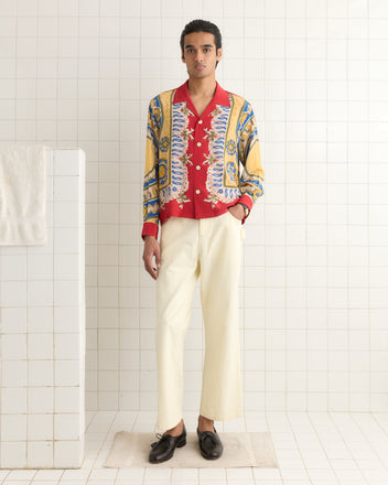 A person wearing a Bricolage Long Sleeve Shirt, white pants, and black shoes stands in a tiled room with a towel on a rail.