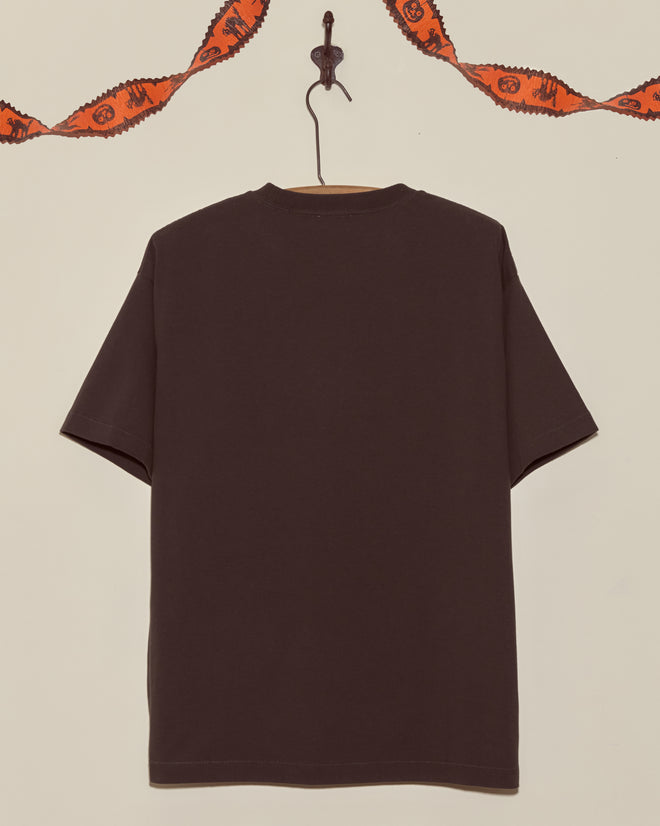 The Bug Tee, a plain black shirt, hangs on a hook while orange Halloween garland decorates the wall above, creating a festive showcase for this classic Halloween tee.