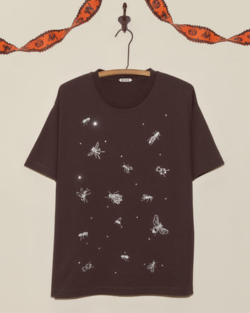 The Bug Tee is a black shirt with white insect illustrations, shown on a hanger with orange garland in the background—an ideal vintage choice for kids who love Halloween and unique tees.