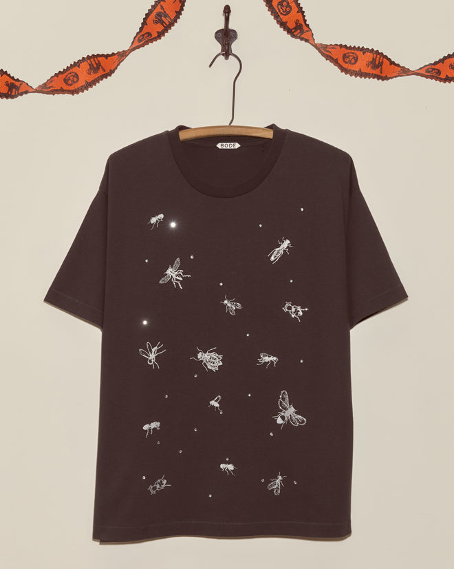 The Bug Tee is a black shirt with white insect illustrations, shown on a hanger with orange garland in the background—an ideal vintage choice for kids who love Halloween and unique tees.