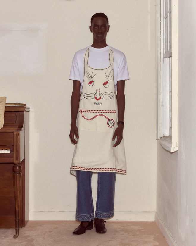 Person wearing a white T-shirt, blue jeans, and a whimsical Bunny Apron featuring a cute bunny face design, standing indoors.