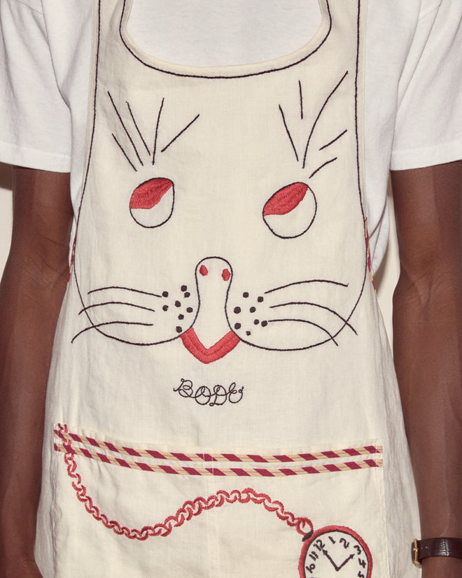 Someone is wearing a Bunny Apron, a linen apron featuring a stitched cat face and a clock design near the pocket.