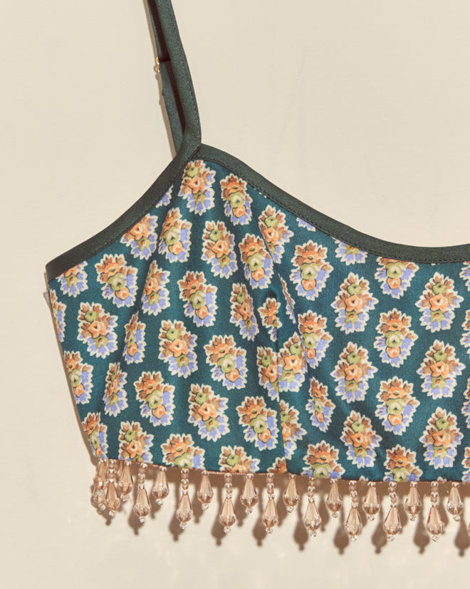 The Beaded Bouquet Bra is a unique floral crop top bralette with beaded tassels along the hem, shown against a beige background.