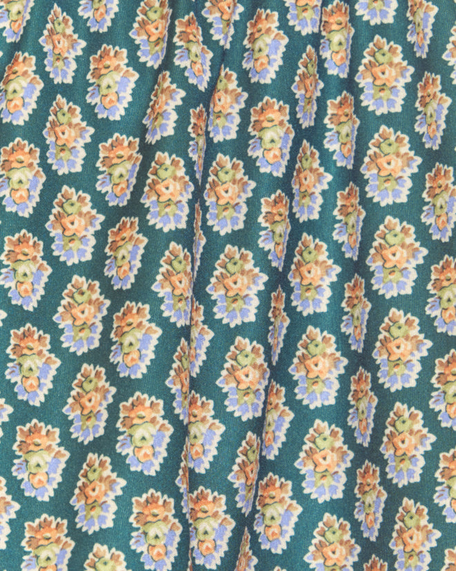 The Beaded Bouquet Shorts feature teal fabric with a repeating floral pattern of small orange and yellow clusters with green leaves, crafted from deadstock yardage—ideal for unique tap shorts.