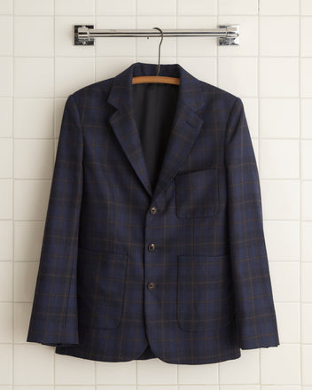 The Bunting Plaid Suit Jacket - 38, a unique sport coat made from 100% wool, hangs elegantly on a wooden hanger against the tiled wall.