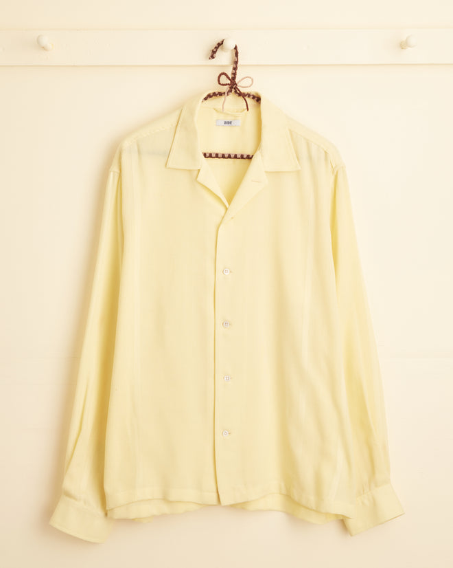 The Cadmium Yellow Line Shirt - XL/XXL, a light yellow long-sleeve button-up featuring custom textiles, is hanging on a white wall hook.