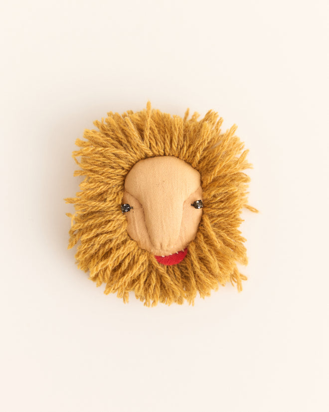 The Calder Leo Brooch features a handmade lion face with a yarn mane, button eyes, and a red felt mouth, inspired by Alexander Calder jewelry and the whimsy of Calder’s Circus brooch.