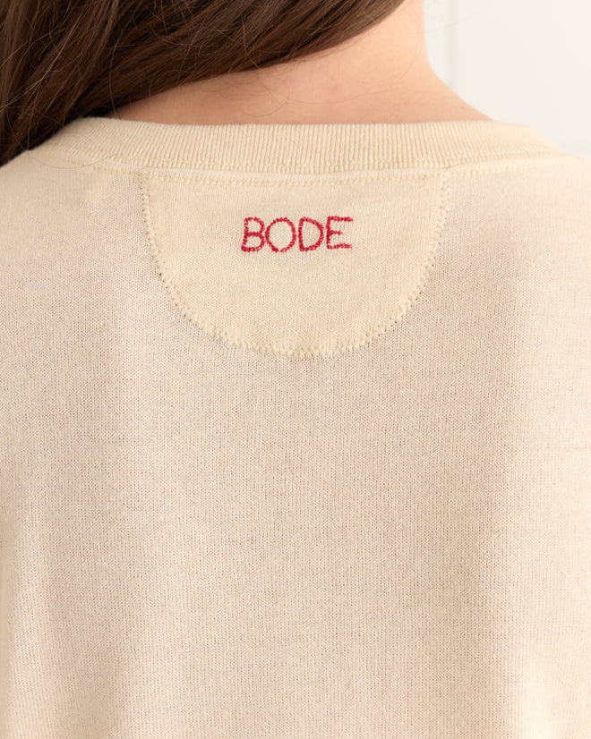 Close-up of the back of the cream-colored Campus Henley sweater, crafted from organic cotton, featuring the elegantly embroidered "BODE" logo in red on the neckline.