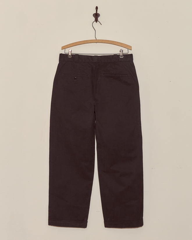 Campus Trousers in black, made from heavyweight cotton twill, are displayed on a wooden hanger against a plain white wall.