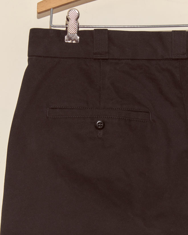 Close-up of the Campus Trousers - Black in heavyweight cotton twill, hanging on a hanger and showcasing the buttoned back pocket, inspired by classic American collegiate style.