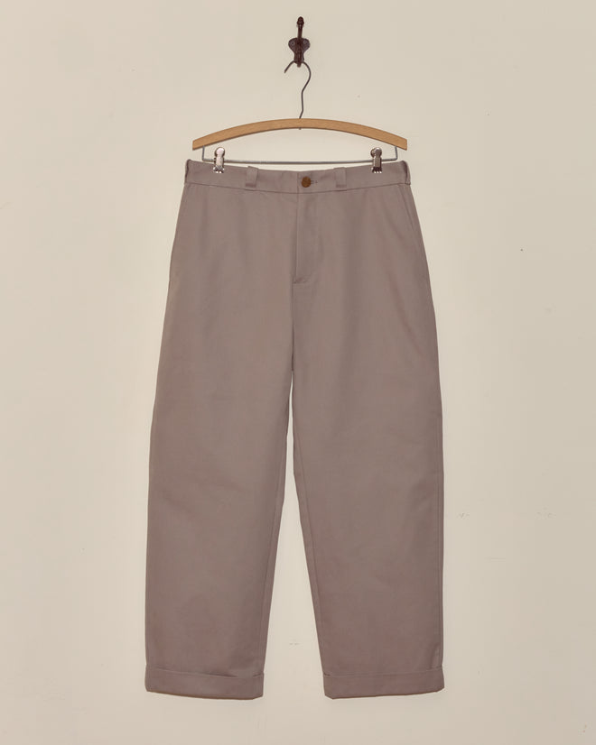 Grey straight-leg Campus Trousers with cuffs, crafted from heavyweight cotton twill, hang on a wooden hanger against a plain white wall for an effortlessly collegiate style look.
