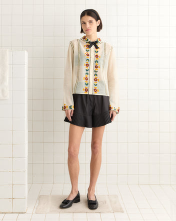 A person in a Candyfloss Blouse, black shorts, and loafers stands in a tiled room.