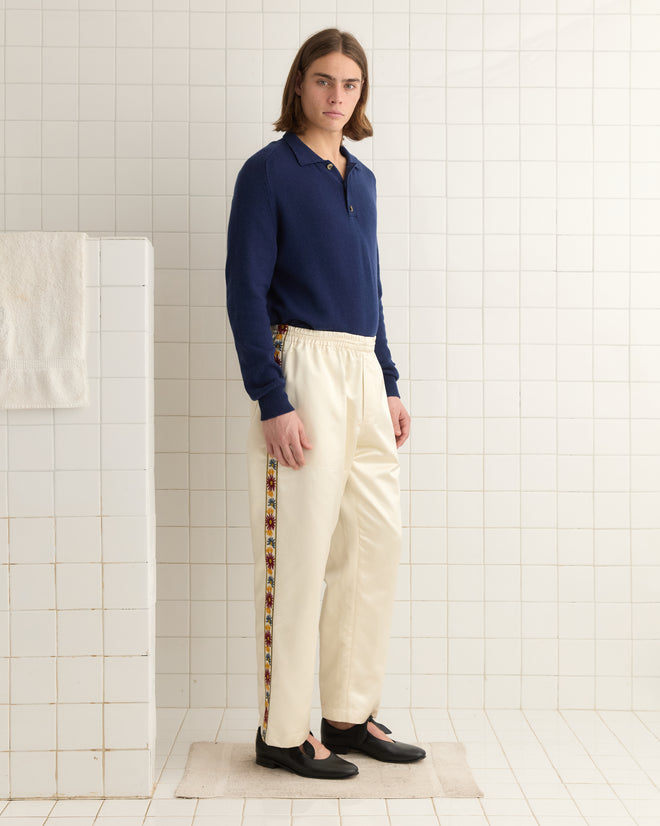 A person in a navy top and Candyfloss Track Pants with embroidered floral trim stands on a mat in a tiled room.