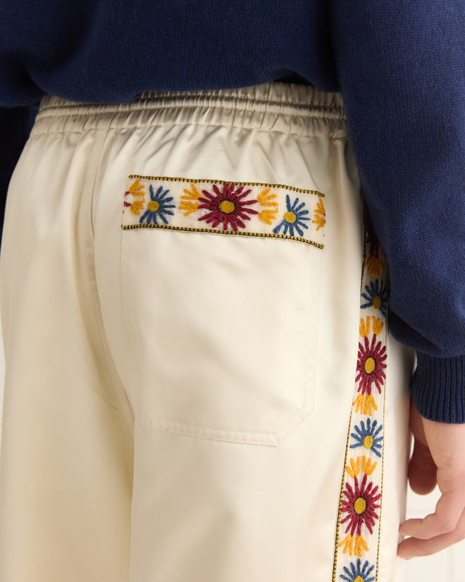 Close-up of Candyfloss Track Pants in ivory with colorful yarn embroidery on the pocket and side stripes, paired with a navy top.