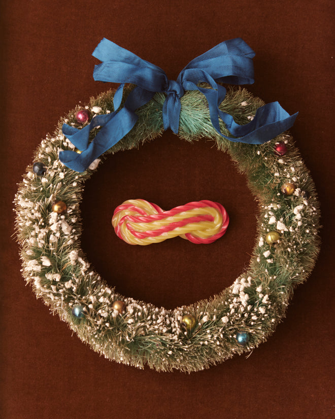 Introducing the Candy Twist Brooch, a delightful piece featuring a blue bow and colorful ornaments, centered around a candy cane motif against a brown backdrop, evoking the charm of vintage jewelry.