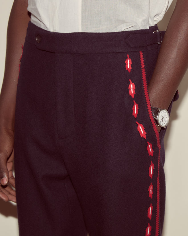 Wearing Carroll Side-Buckle Trousers with red embroidery, a watch, and a partially visible white shirt—an Alice Through the Looking Glass-inspired look.