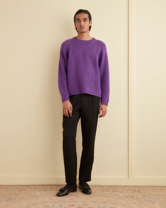 A person in a Cashmere Crewneck - Purple and black pants stands against a cream-colored wall.