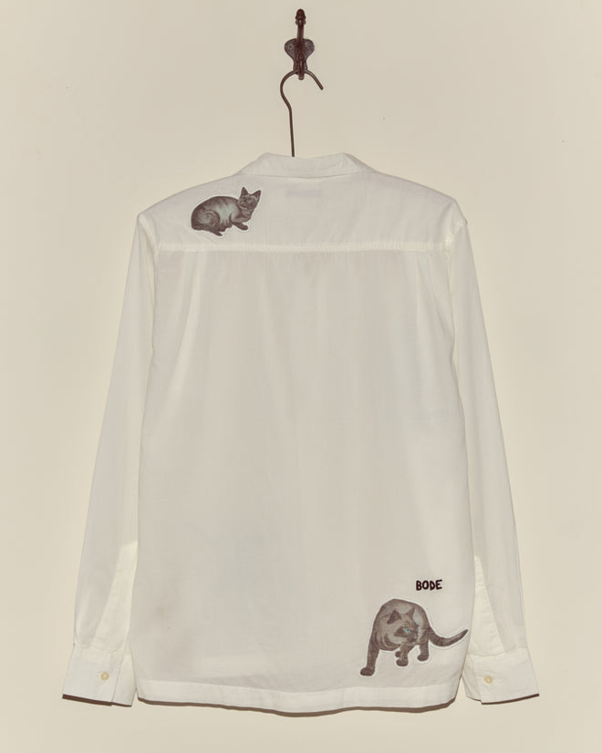 Cat Motif Long Sleeve Shirt—white, vintage-inspired, with playful cat illustrations on the shoulder and near the hem; button-up style shown on a hanger.