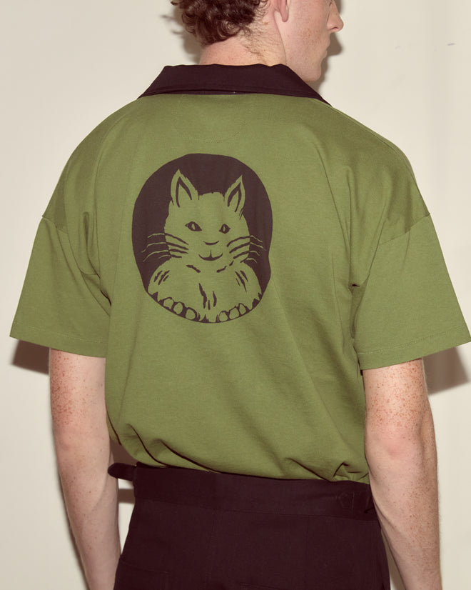A person, seen from behind, is wearing the Cat Polo - Green, which features a black cat face graphic on the back.