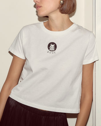 Woman wearing the Cat Tee, a vintage-weight cotton shirt featuring a cat graphic, paired with large pearl earrings, facing sideways.