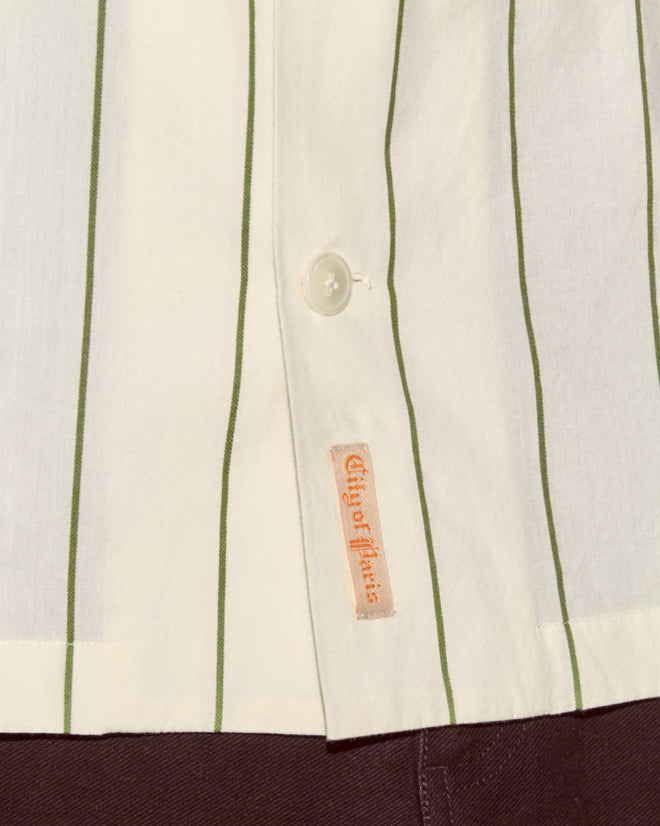 Close-up of the Celery Stripe Short Sleeve Shirt, featuring white fabric with green stripes, button detailing, and a vintage-inspired "City of Athaus" label near the hem.