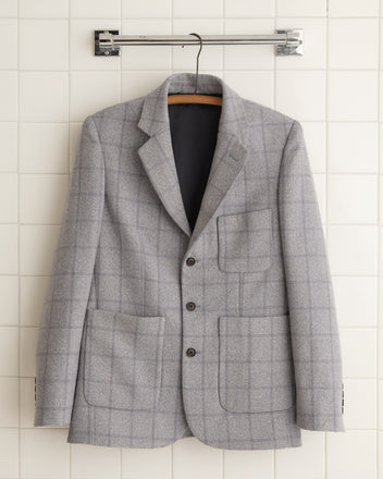 The unique Cement Block Suit Jacket - 36 is showcased hanging elegantly against a tiled wall, reminiscent of 1960s suiting fabric.