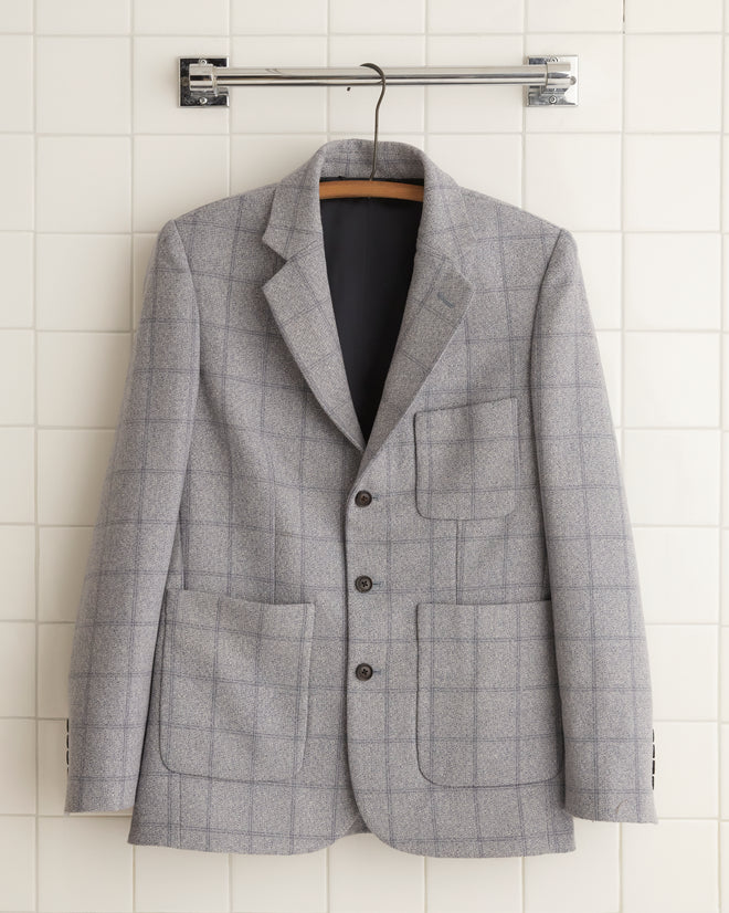 The unique Cement Block Suit Jacket - 36 is showcased hanging elegantly against a tiled wall, reminiscent of 1960s suiting fabric.