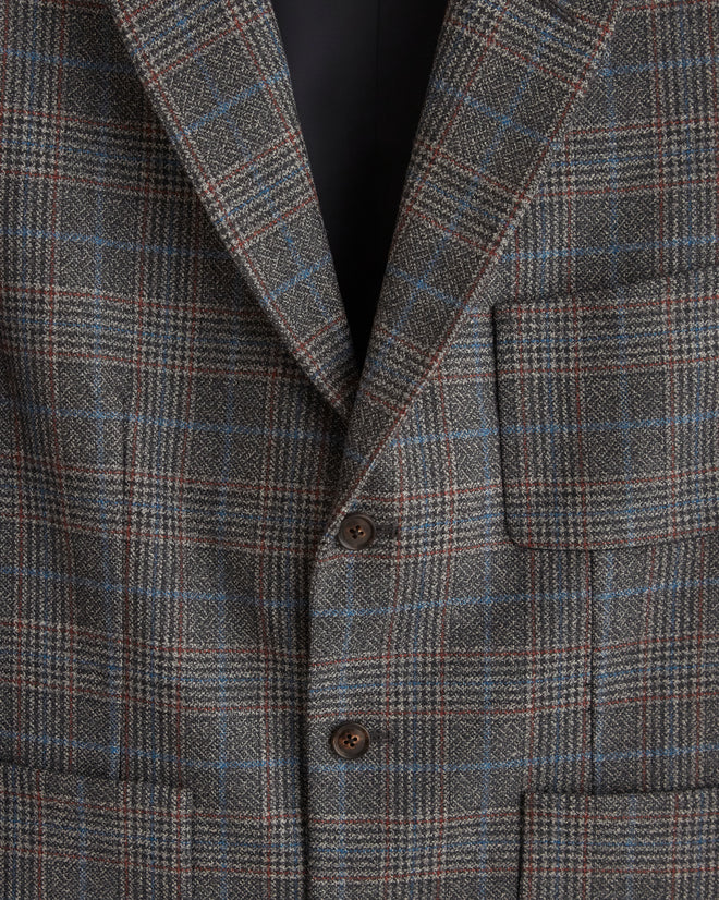 The Cannery Plaid Suit Jacket - 44, crafted from fine suiting fabric, hangs elegantly on a wooden hanger against a white tiled wall.