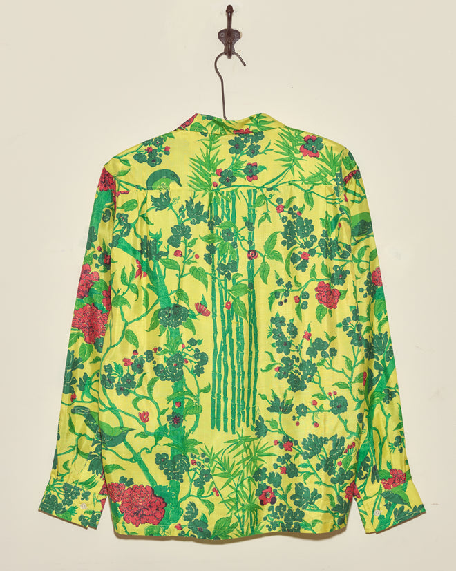 The Chartreuse Jungle Shirt (M/L), a bright yellow vintage long-sleeve with a green and red floral and bamboo pattern, hangs on a hook.