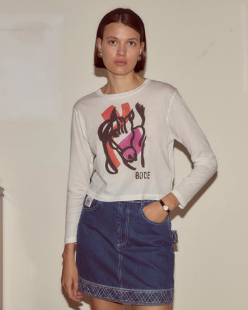 Woman wearing the Cheval Long Sleeve Tee with abstract colorblocking and a blue denim skirt, standing against a beige wall.