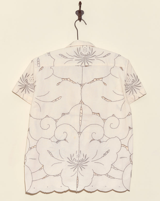 Chrysanthemum Carpet Short Sleeve Shirt in XS—white with bold floral patterns—displayed on a hook against a cream wall.