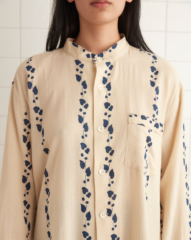 A person wearing the Climbing Ivy Tunic, inspired by the 1920s-1930s block-printed designs, paired with black tights stands in a tiled room, with a 100% cotton towel resting on the ledge.