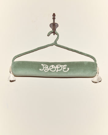 A teal Cloakroom Hanger holds a green velvet draft stopper with white tassels and 