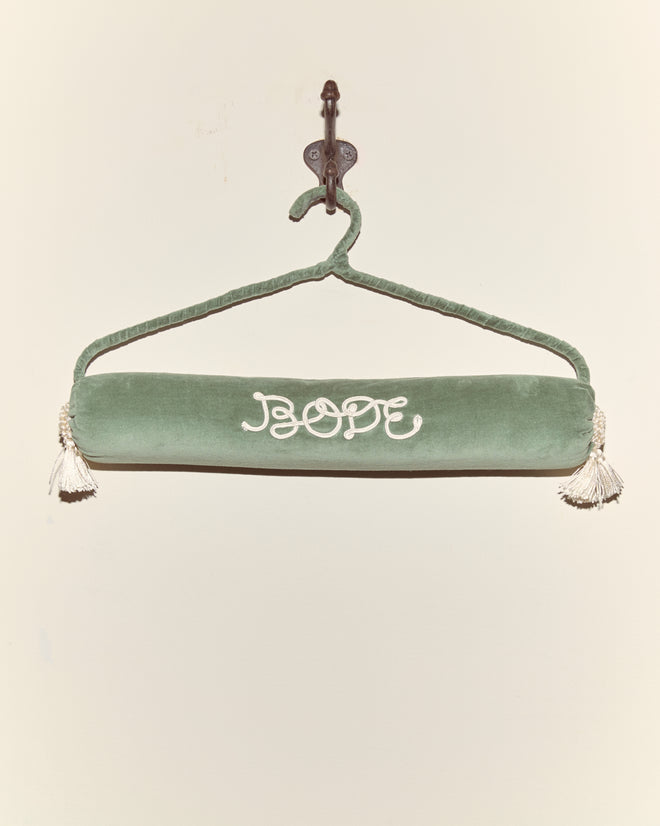 A teal Cloakroom Hanger holds a green velvet draft stopper with white tassels and 