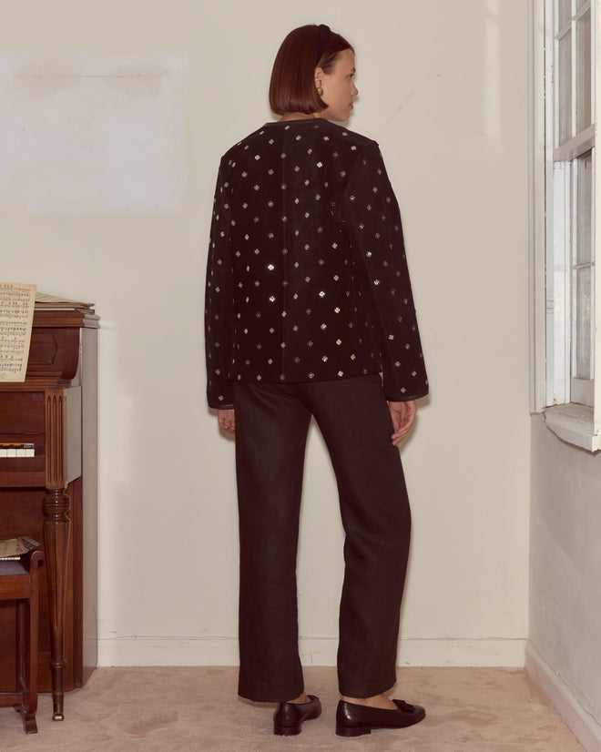 A woman stands by a piano near a window, facing away, wearing the Clover Charm Jacket with its vintage-inspired boxy silhouette.