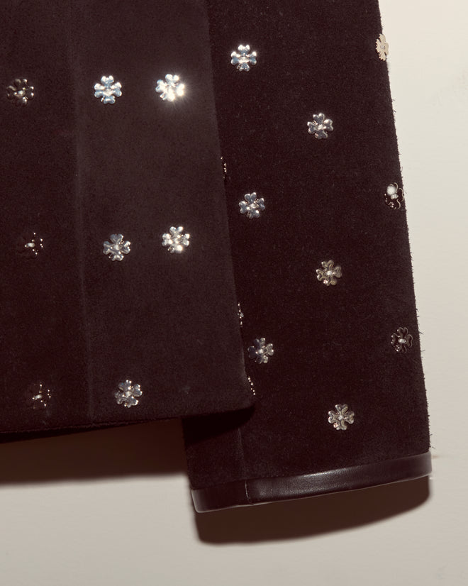 Close-up of the Clover Charm Jacket—a black suede style featuring shiny, silver flower-shaped embellishments and a boxy silhouette.