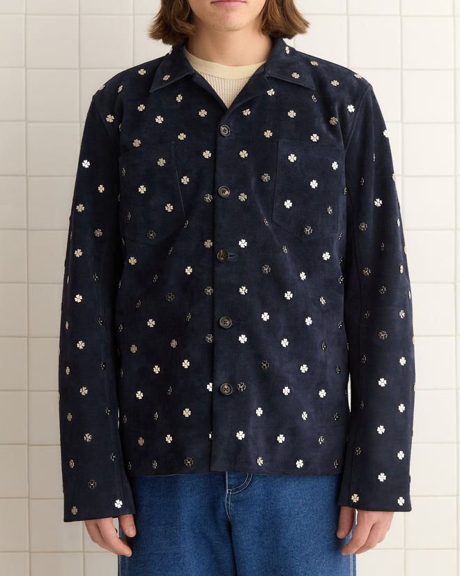 Person wearing a dark navy Clover Work Shirt with floral patterns, paired with blue jeans and silver clover charms, stands in front of a tiled wall.