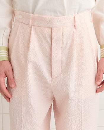 The person is wearing Club Stripe McNab trousers in pink and white with a textured seersucker finish and a white shirt accented with green cuffs.