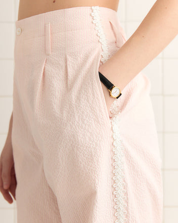 Person wearing Club Stripe Murray Trousers in Pink/White with a black watch, hand placed in pocket.