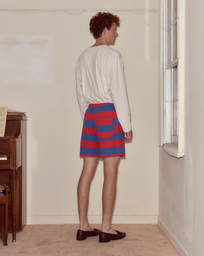 A man wearing a long-sleeve shirt, Clubhouse Shorts, and loafers stands facing a corner of a room.