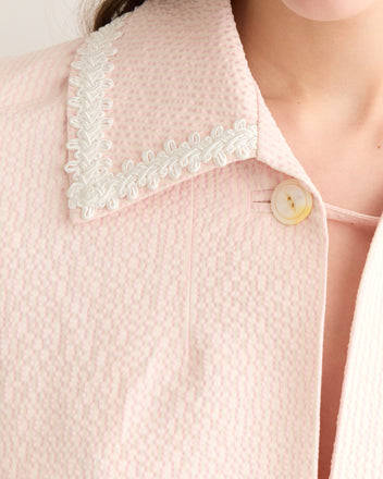 A close-up of the Club Stripe Swing Jacket showcases its decorative collar and antique pearl button, exuding a 19th-century-inspired charm with its pink seersucker fabric.