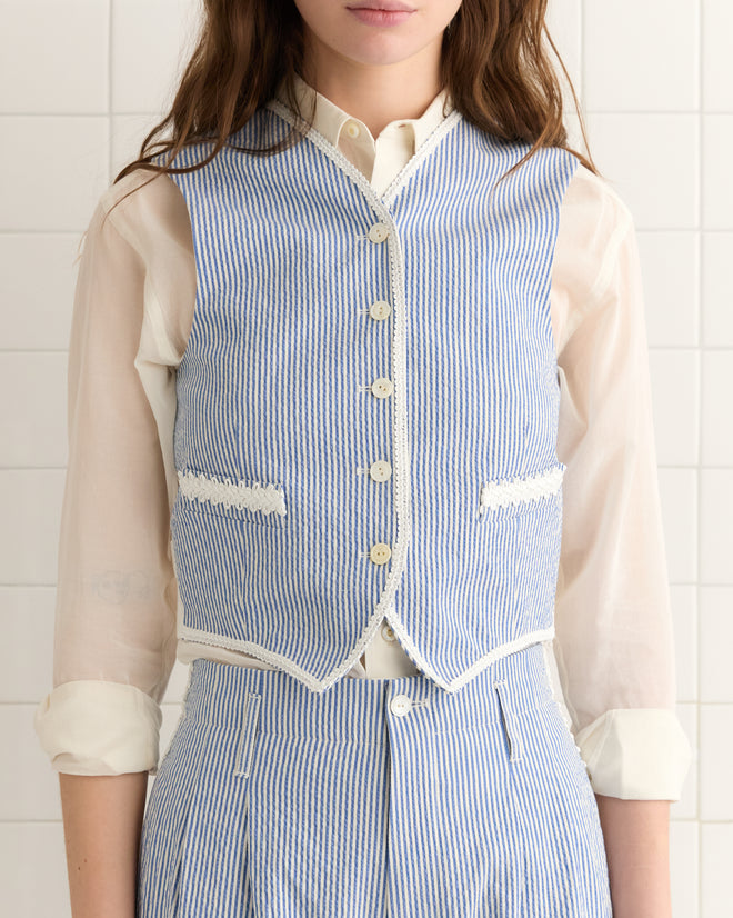 Woman wearing the Club Stripe Waistcoat in blue and white, styled with matching high-waisted pants and a sheer white blouse.