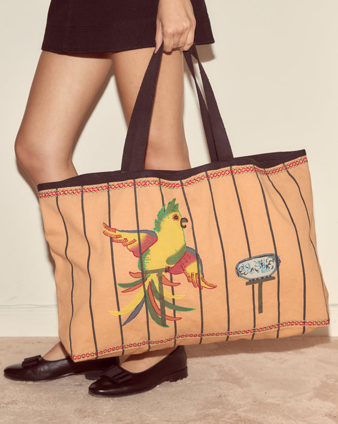 A person carries the Cockatoo Large Tote, featuring a colorful parrot and black stripes, styled with a skirt and black flats.