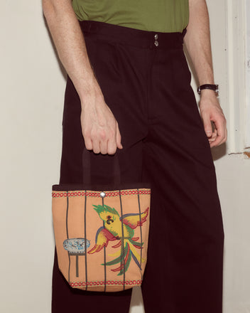 A person in black pants holds the Cockatoo Small Tote, featuring a colorful painted cockatoo design, with a green shirt visible.