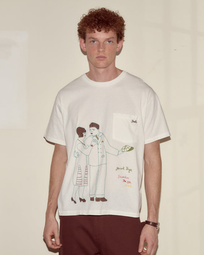 A man with curly hair wears the Companion Tee, a 100% cotton white t-shirt featuring an illustrated couple and handwritten text.