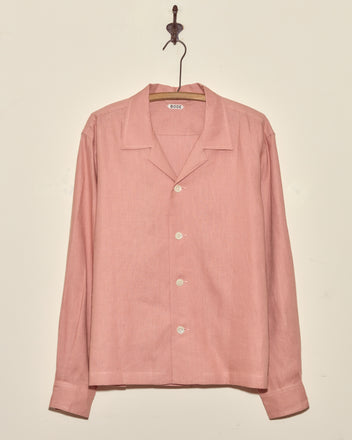 The Conch Shell Shirt - L is a light pink deadstock linen, long-sleeve button-up, displayed on a hanger against a plain beige wall.