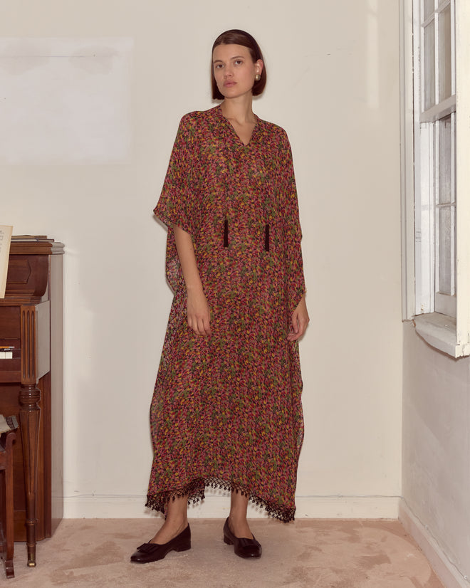 A woman wearing the Confetti Floral Kaftan stands indoors by a window and a piano, looking at the camera.