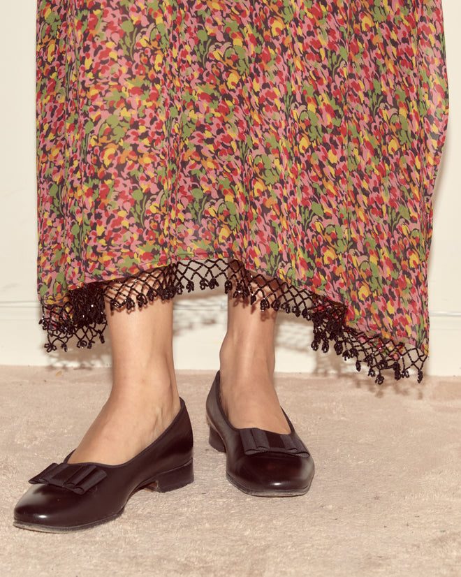 A person in the Confetti Floral Kaftan, featuring a beaded tassel hem, and black loafers stands on a carpet.