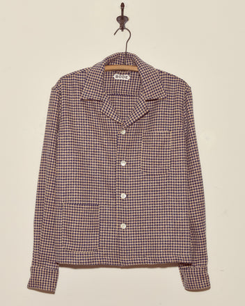 The Confetti Houndstooth Overshirt - S/M, a collared button-up made from deadstock wool, hangs on a wall hook.